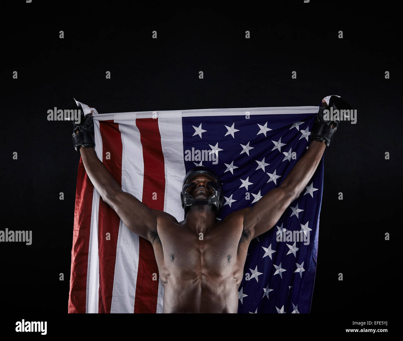 Young boxer carrying american flag raised in victory on black background. American boxing champion celebrating success. Stock Photo