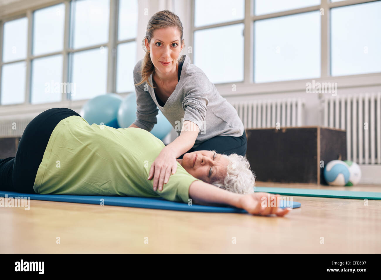 Elderly woman being helped by her personal instructor in the gym for exercising. Female trainer assisting senior woman in her ph Stock Photo