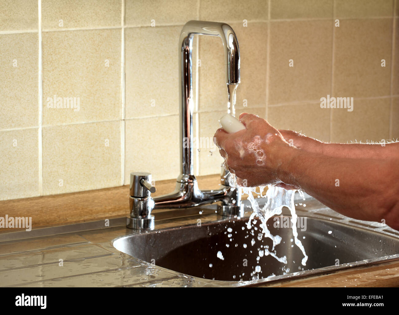 A man washes his hands under a running  faucet; this image is back lit to show detail in the water Stock Photo
