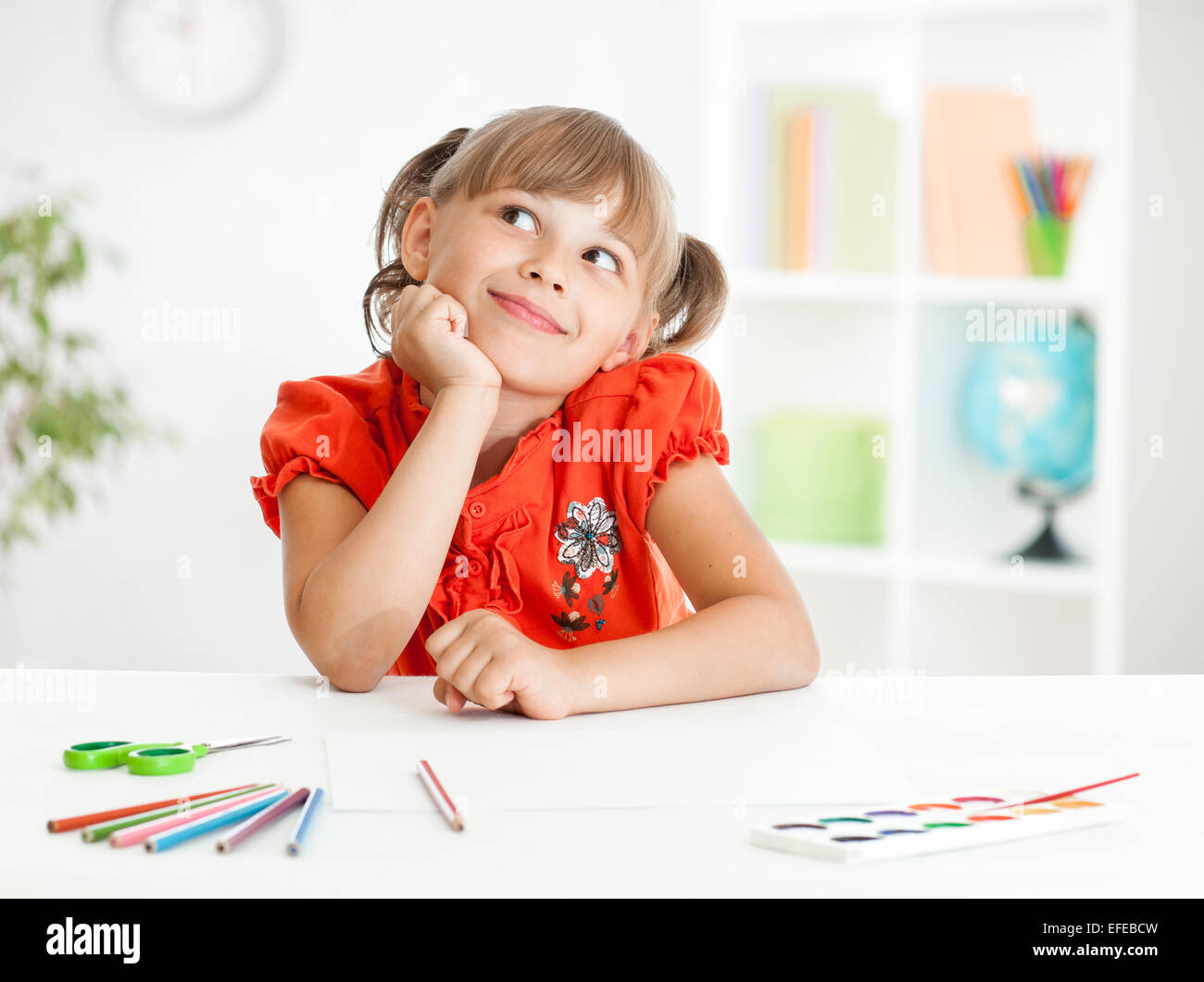 Smiling cute schoolgirl dreaming making homework. Creation concept. Stock Photo