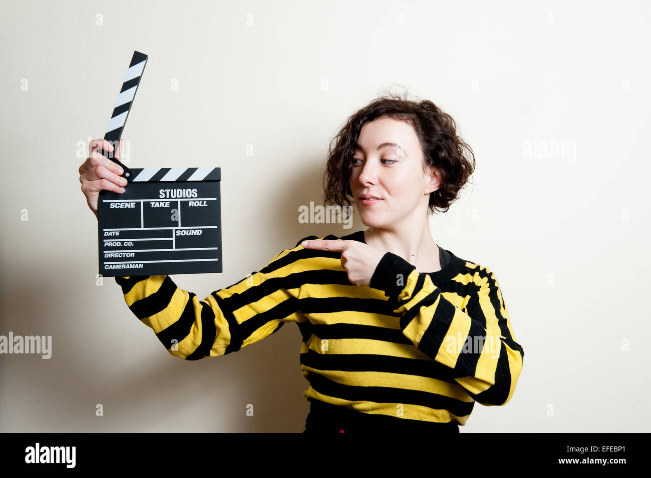 Girl in yellow t-shirt with smiling face pointing out a movie clapper on white background Stock Photo