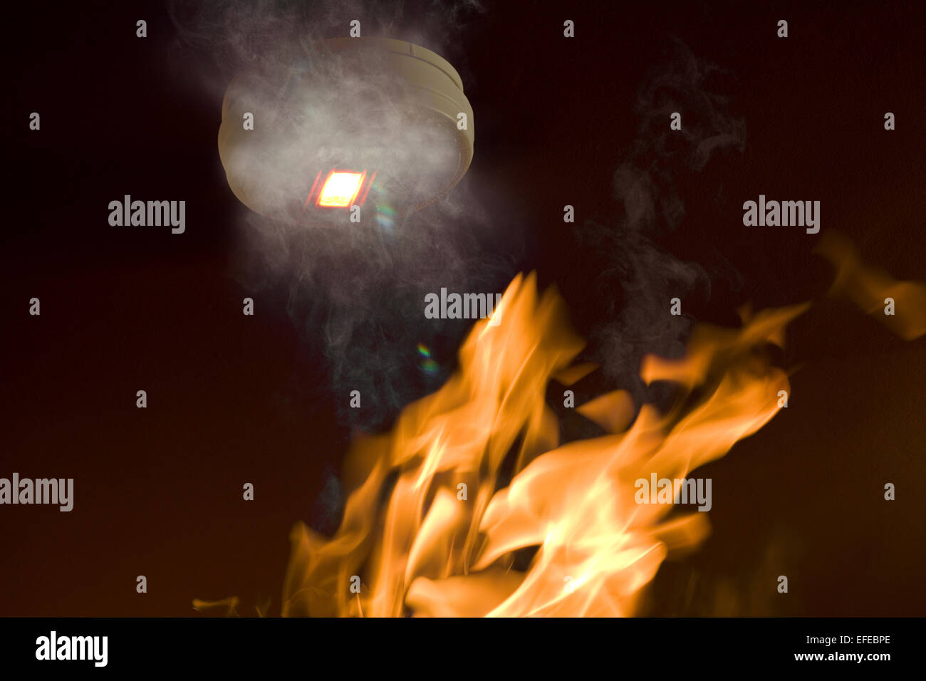 A smoke alarm with emergency light activated by smoke, with flame approaching Stock Photo