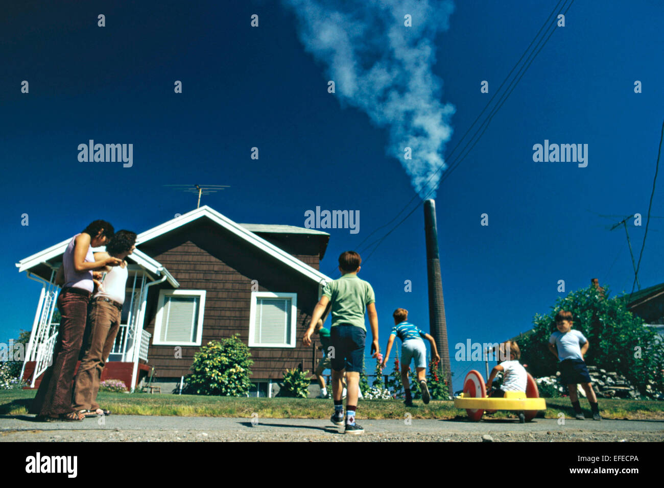 Children play in their yard near the Asarco Company Tacoma copper smelter smokestack belching arsenic and lead pollution August 1972 in Ruston, Washington. Stock Photo