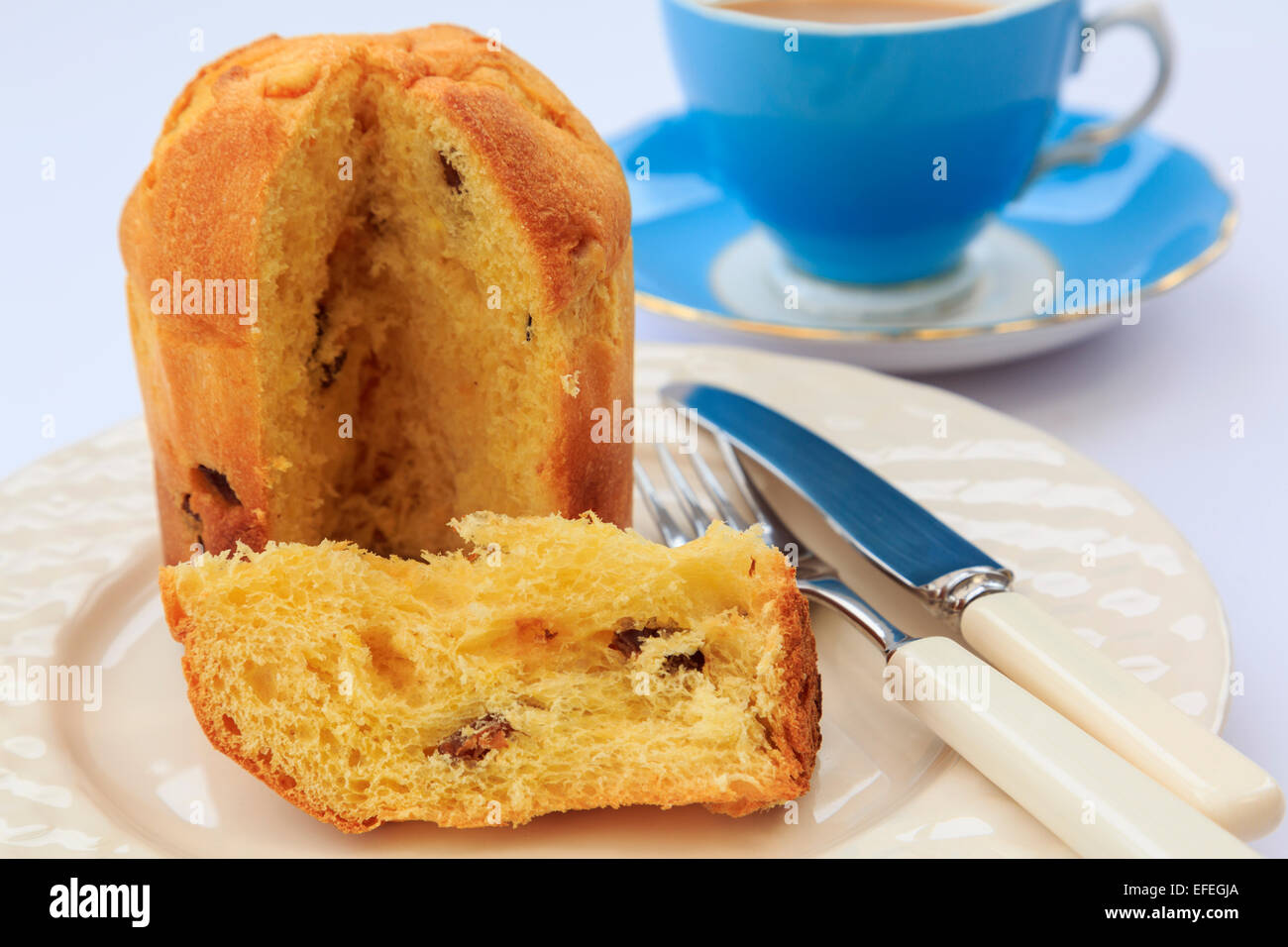 A slice of Panettone Italian Christmas fruit bread cake on a plate for afternoon tea with a blue teacup and saucer on a table top. England UK Stock Photo