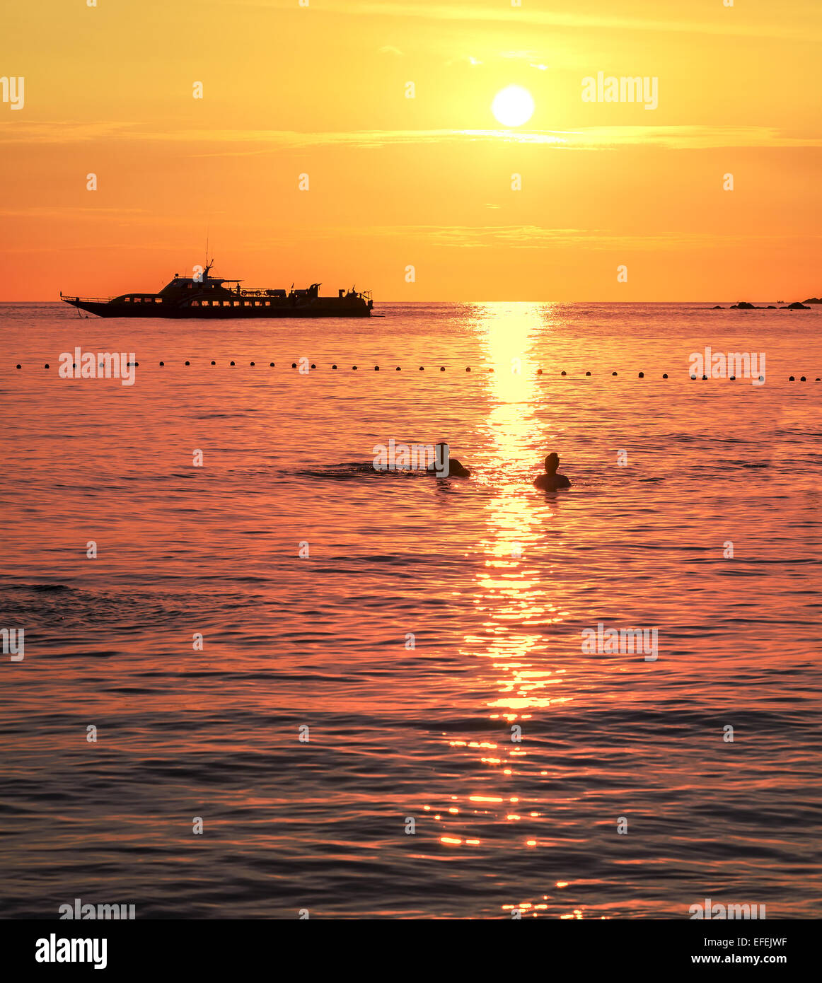 Silhouettes of a swimming couple and ship at sunset. Stock Photo