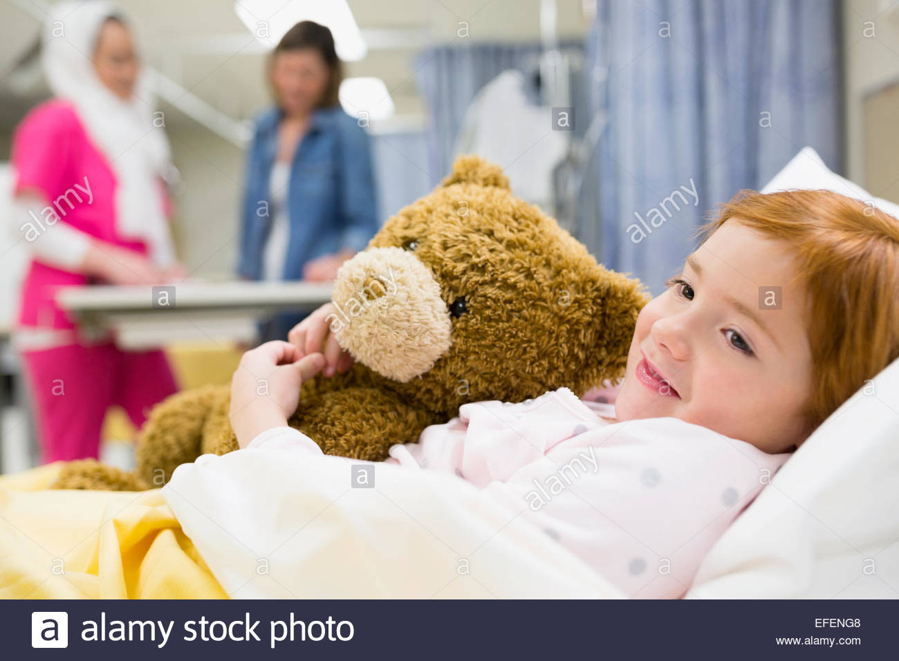 Girl hugging teddy bear in hospital bed Stock Photo