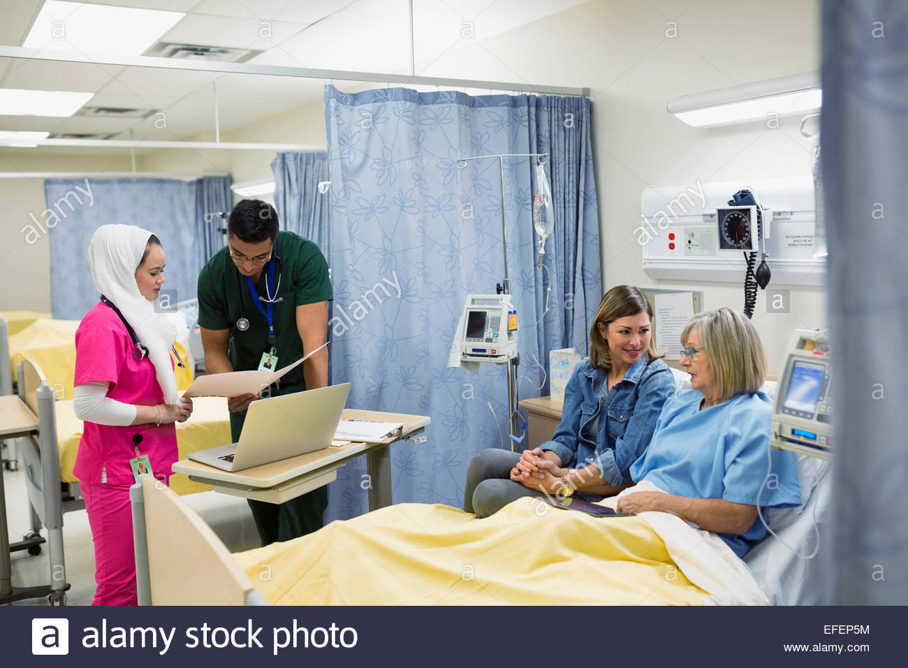 Nurses checking on patient in hospital bed Stock Photo