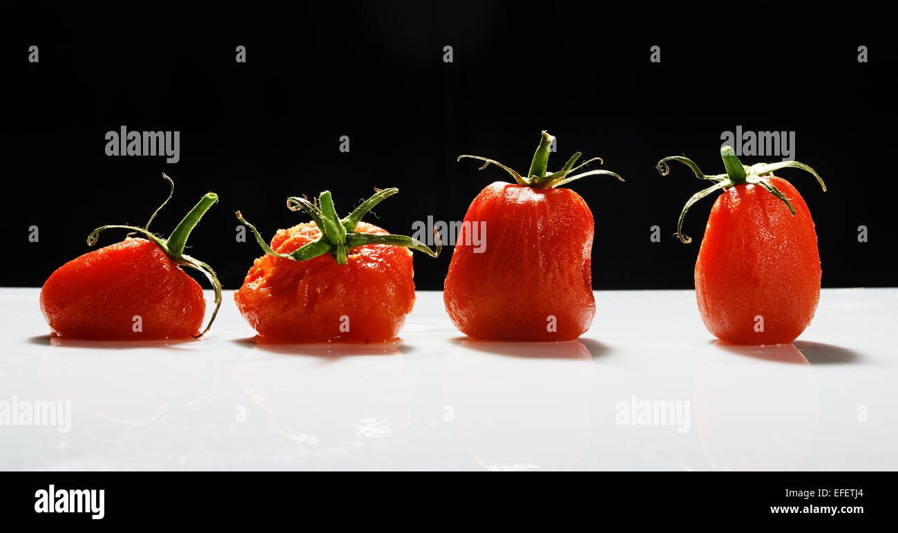 Peeled Tomatoes sitting in a row with black background Stock Photo