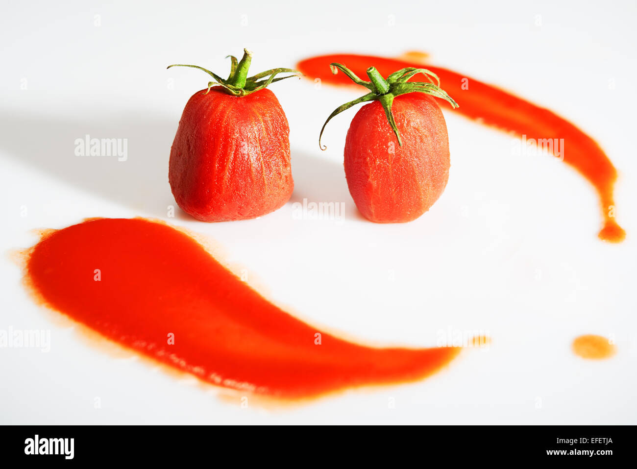 Peeled tomatoes with stems on top and tomato sauce around them Stock Photo