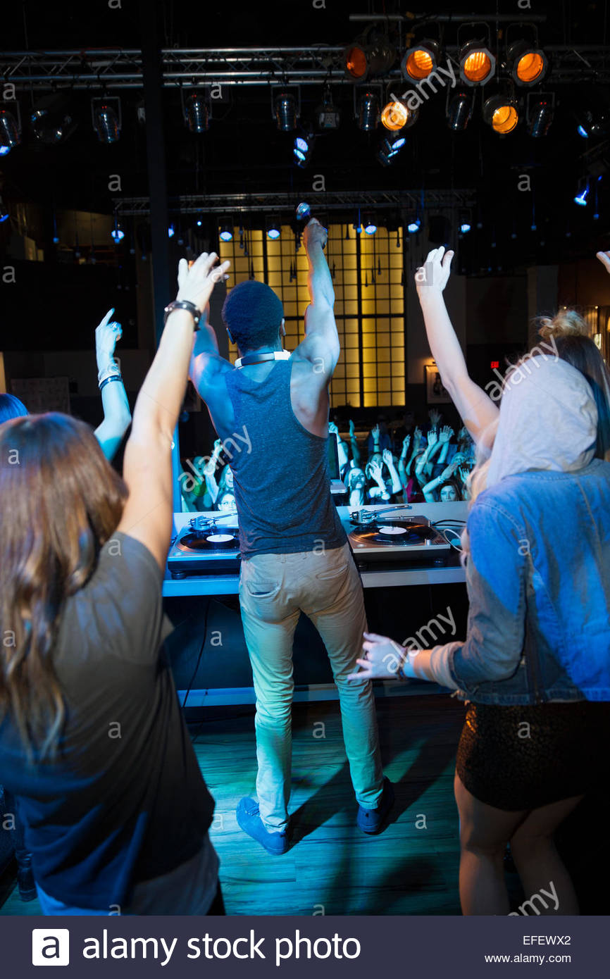 DJ and dancers on stage facing nightclub crowd Stock Photo