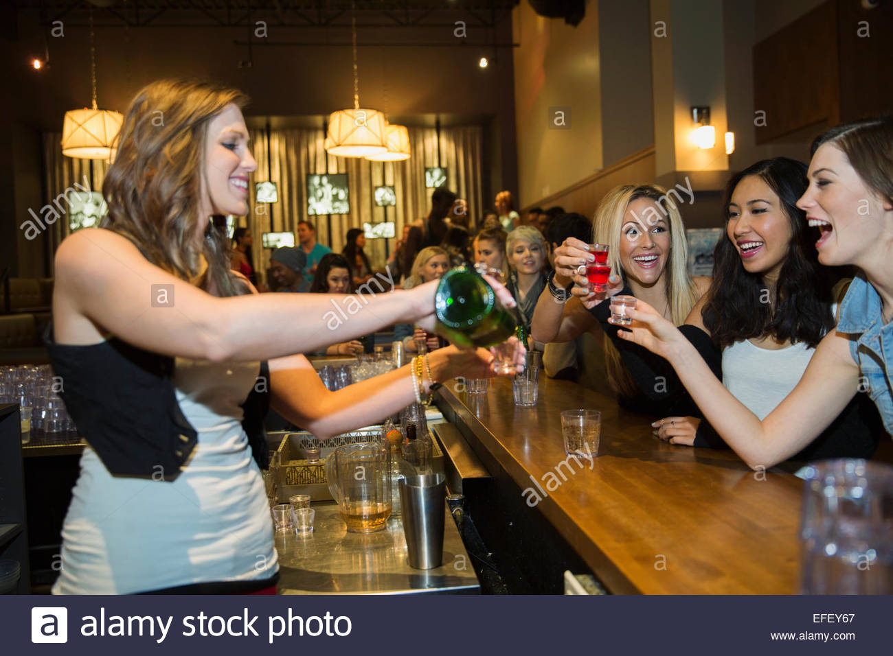 Bartender pouring shots for women at bar Stock Photo