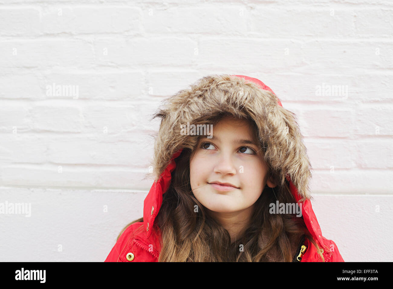 Young girl in red coat thinking and looking up. Stock Photo