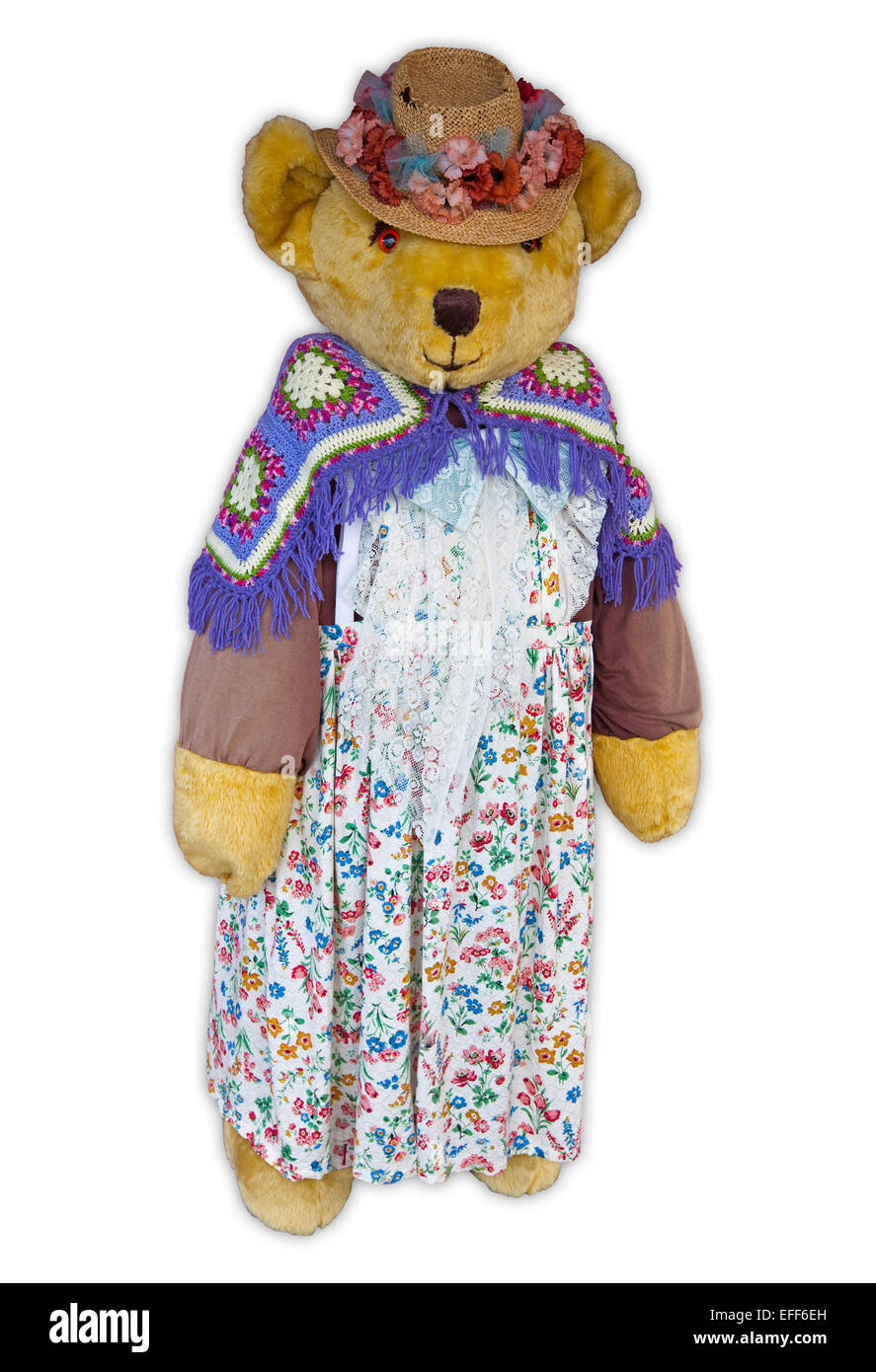 Gigantic life-sized teddy bear wearing floral dress, colourful woollen shawl & straw hat with flowers, against white background Stock Photo