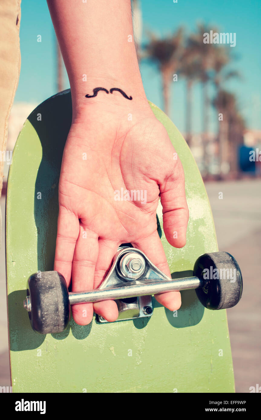 closeup of a young man with a moustache tattooed in his wrist holding a  skateboard Stock Photo - Alamy