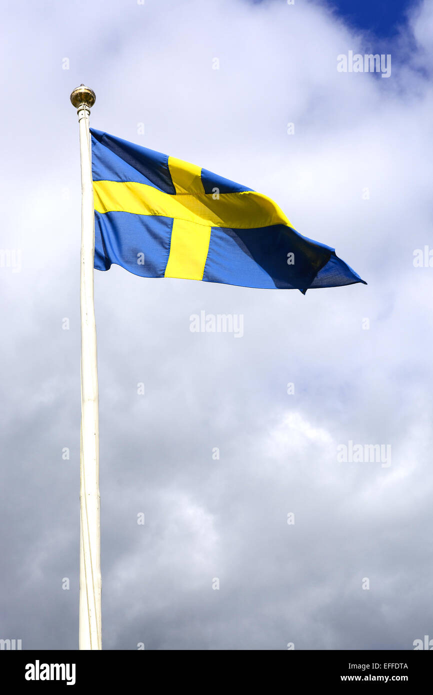 Swedish flag flying in blue with yellow cross against cloudy sky. Stock Photo