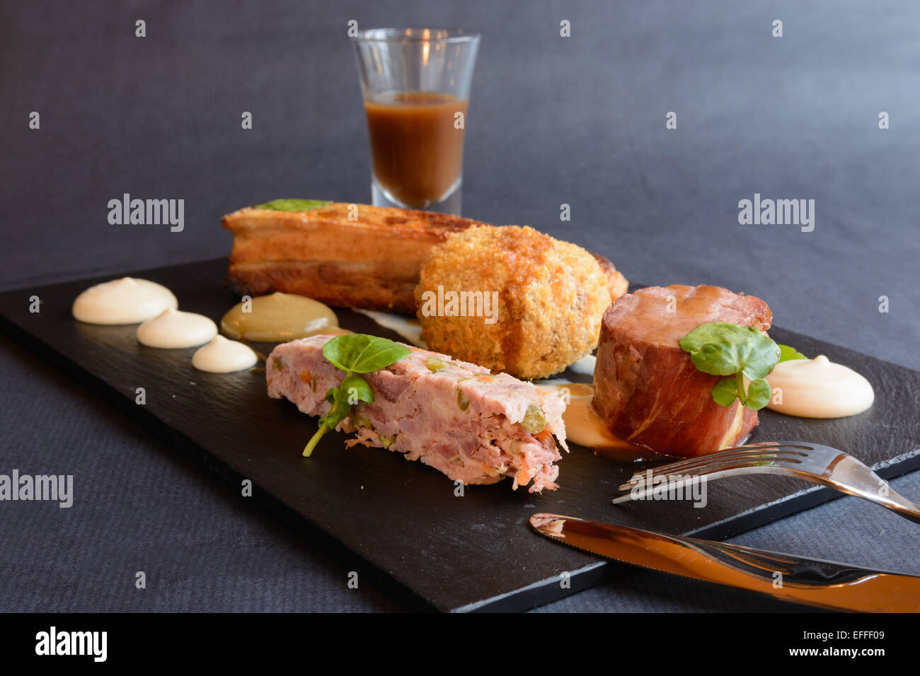 Pork 4 Ways: Sous vide (vacuum cooked) pork loin wrapped in Parma ham, ham hock terrine, pickled vegetables, crisp cider-braised Stock Photo