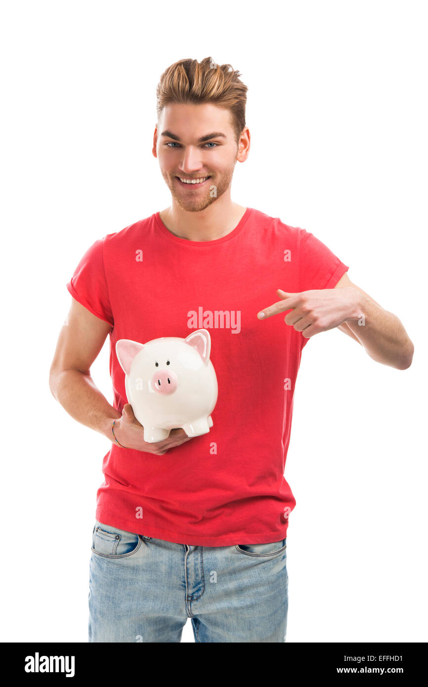 Handsome young man holding and pointing to a piggy bank and smiling ...