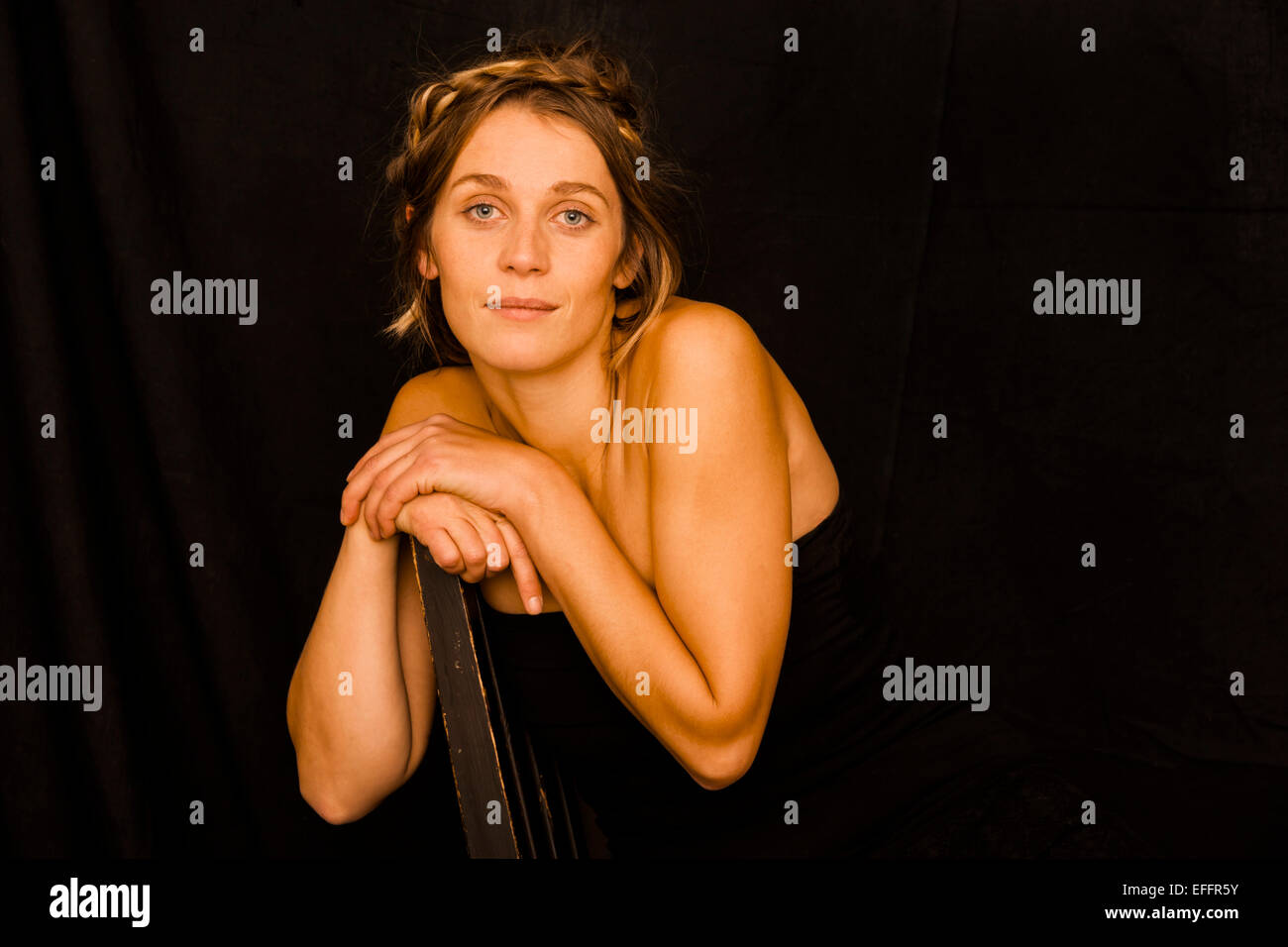 Portrait of woman wearing black corsage leaning on back rest in front of black background Stock Photo