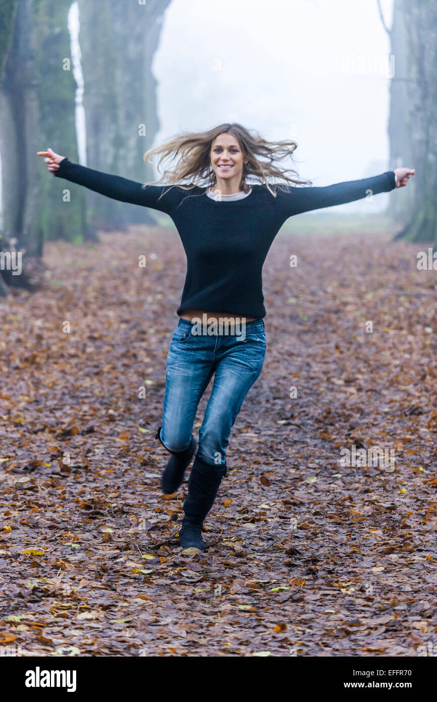 Woman with outstretched armes running along a forest track Stock Photo