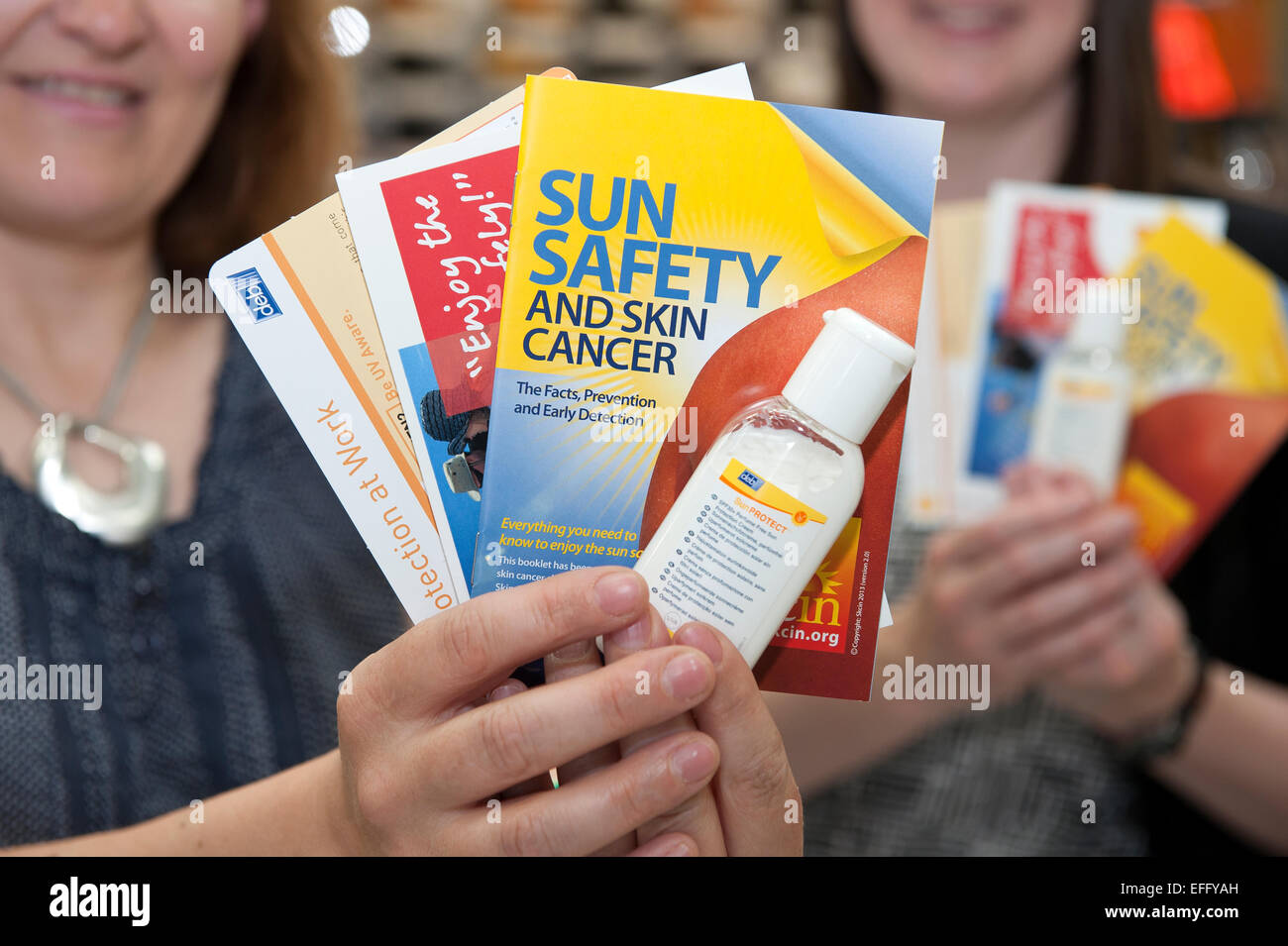 Two unidentified women hold up safety leaflets and sun cream warning about the dangers of skin cancer. Stock Photo
