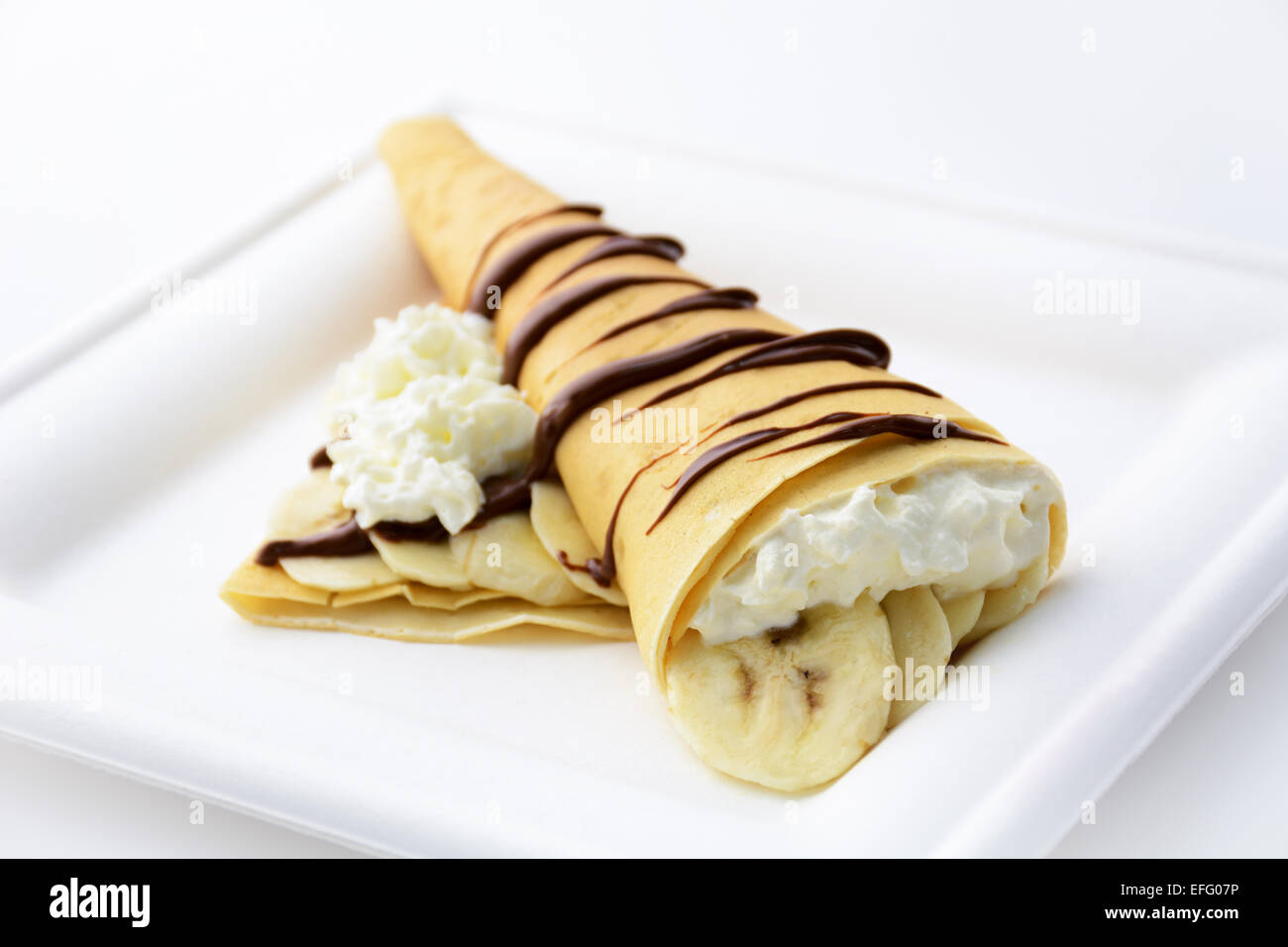 Crepe cone filled with bananas and whipped cream topped with chocolate sauce, isolated Stock