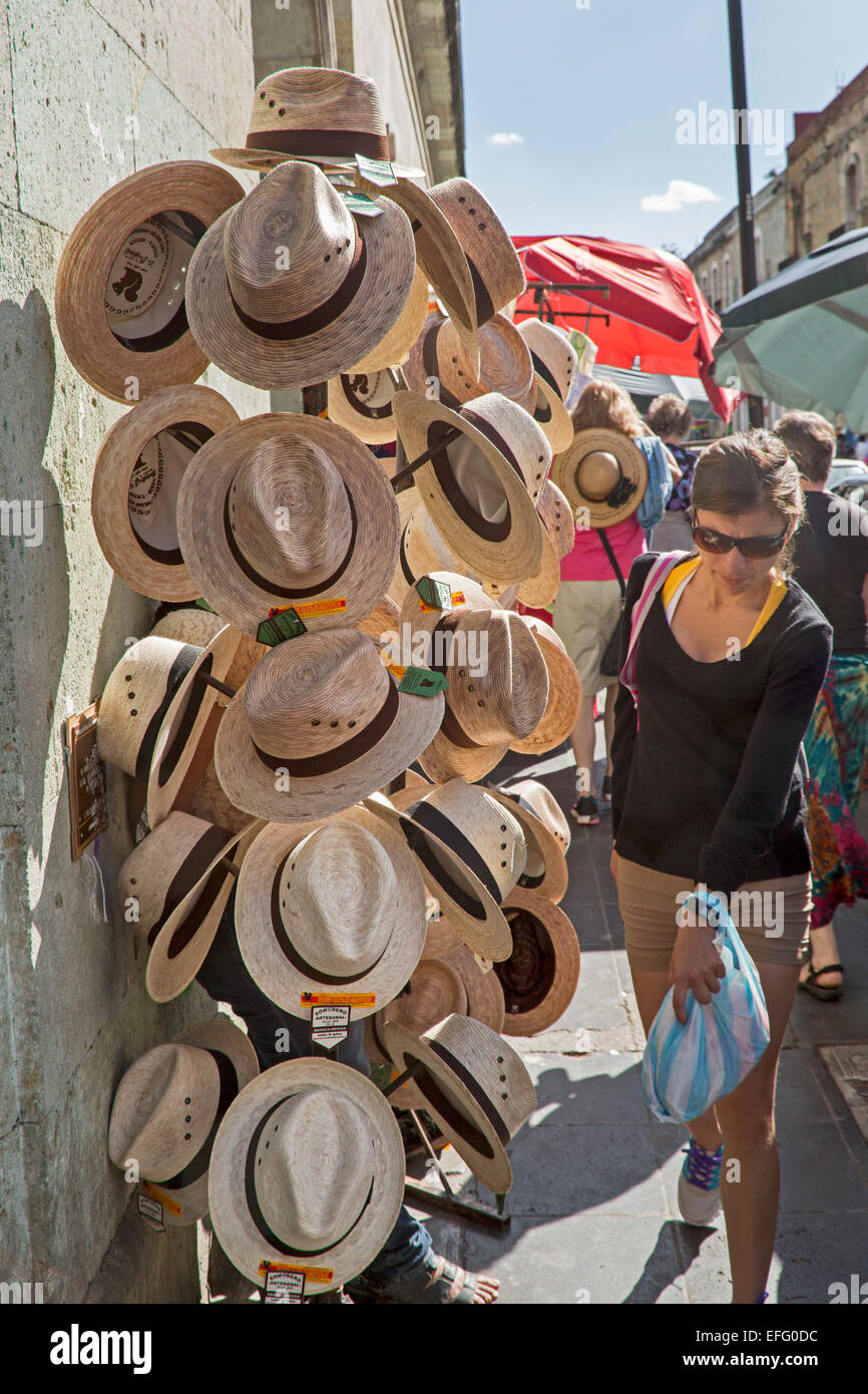 Oaxaca, Mexico - A pedestrian squeezes by a display of hats on sale on a sidewalk. Stock Photo