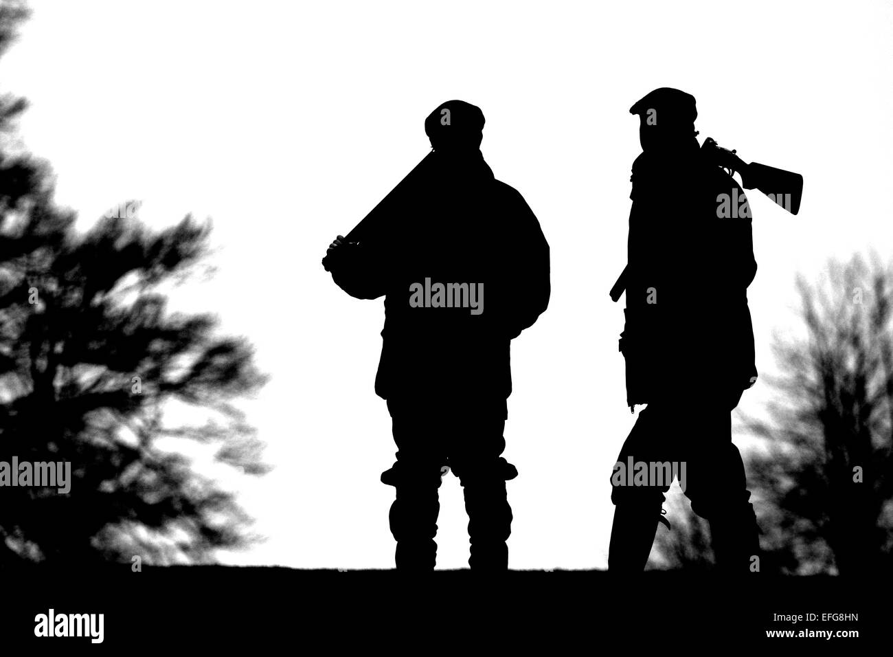 Black and white silhouette of two men carrying shotguns over their shoulder in West Wycombe Park, Buckinghamshire, UK Stock Photo