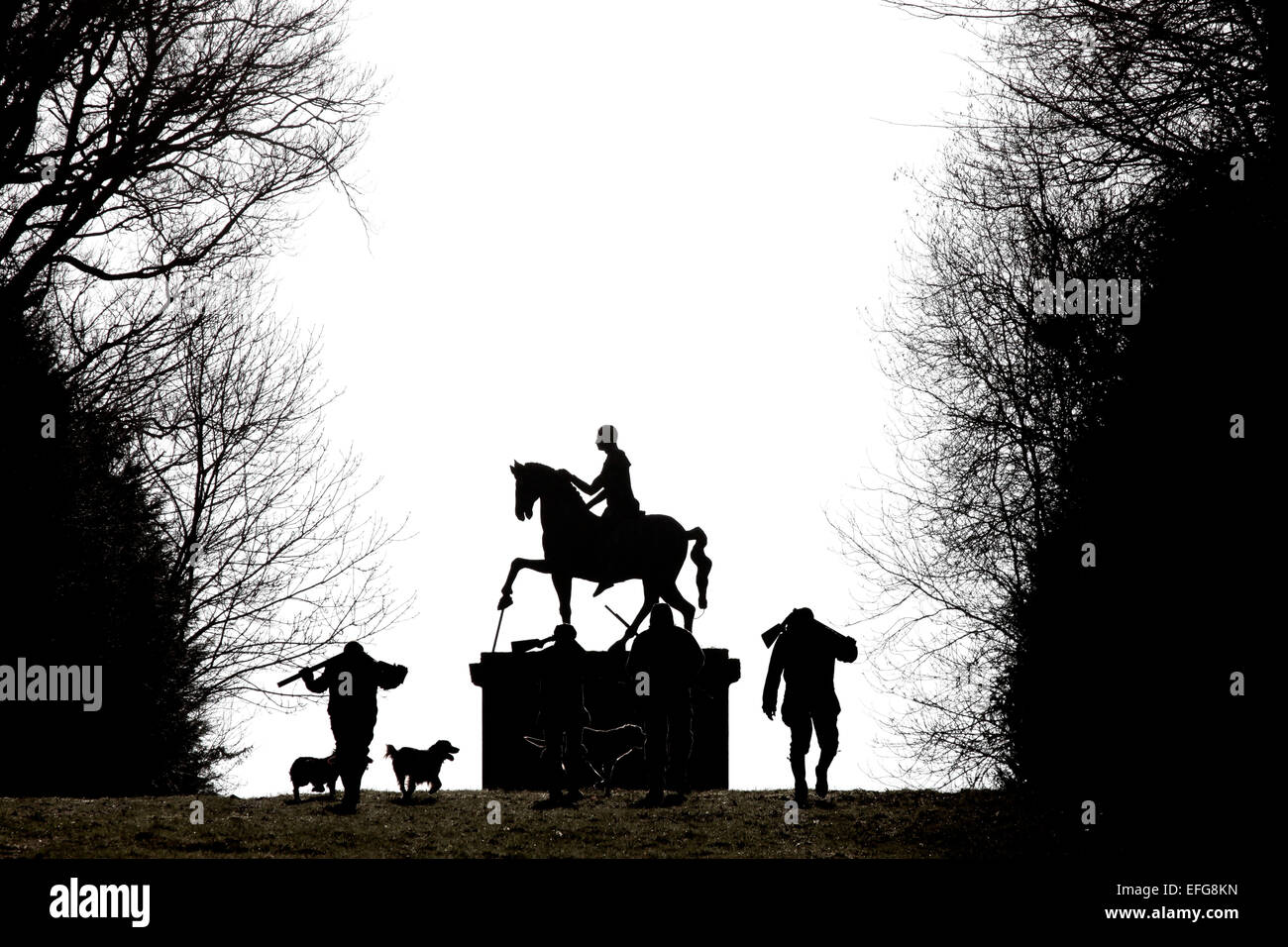 Black and white silhouette of two men and gun dogs by statue of horseman in West Wycombe Park, Buckinghamshire, UK Stock Photo