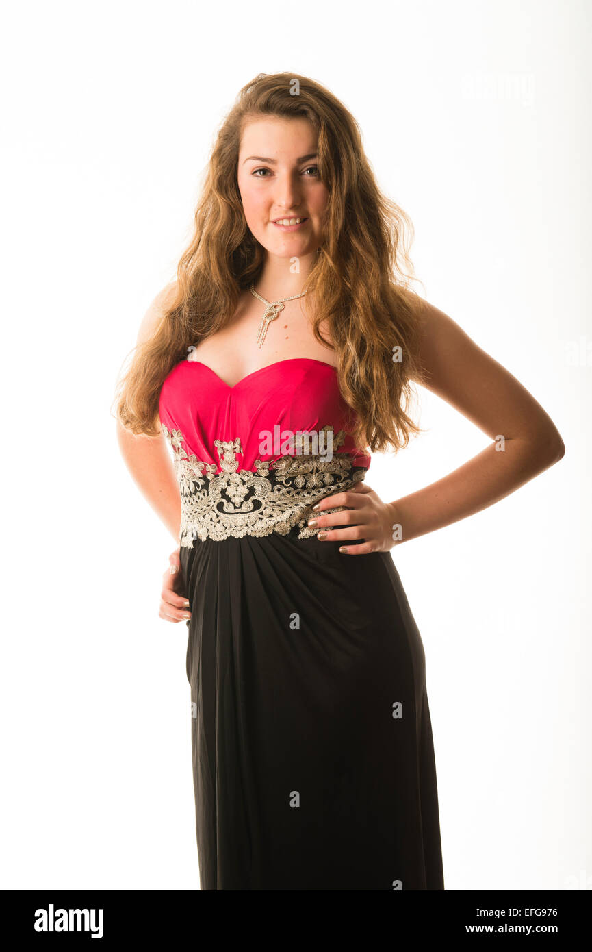 A graceful elegant slim confident fourteen 14 year old teenage girl model with long brown hair, standing with her hands on her hips wearing a dress frock posing in a studio  UK Stock Photo