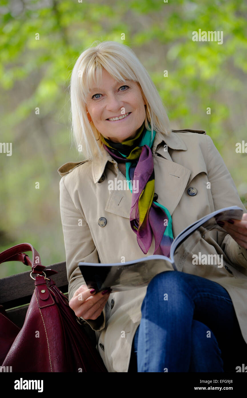 Portrait of a smiling senior woman reading a book sitting on a bench ...