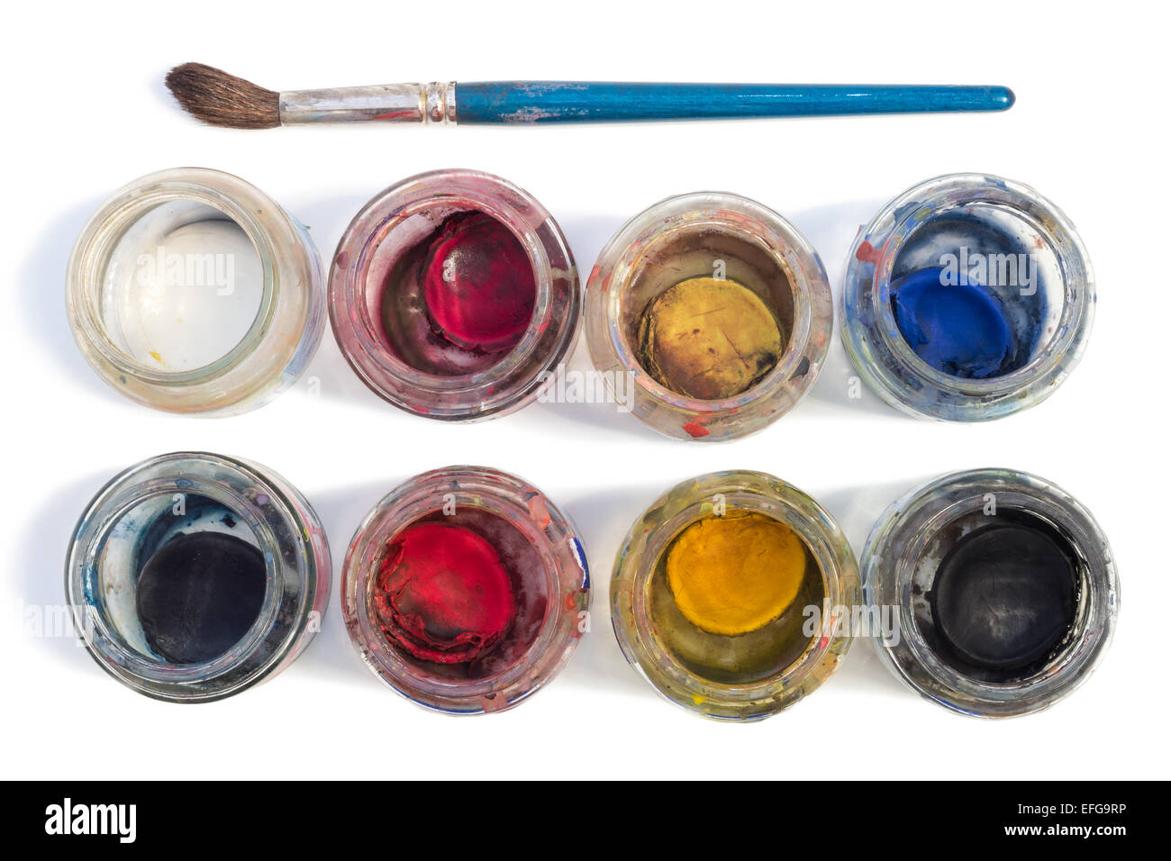 A brush and used watercolors in small glass jars isolated on white background, viewed from above. Stock Photo