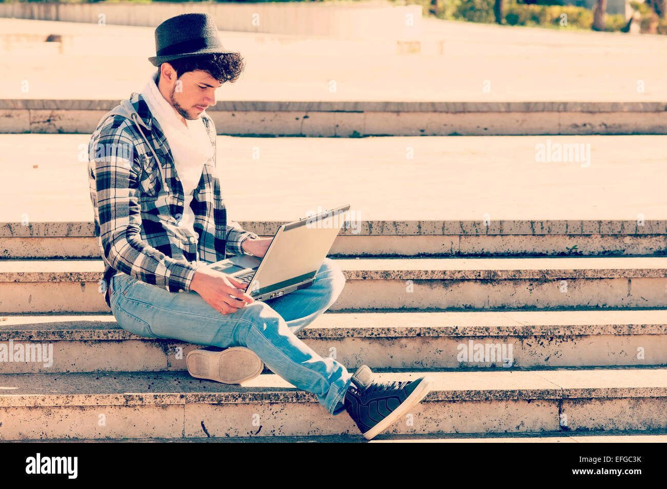 a young boy working on his laptop in an urban environment, iconography of modern mobility with a filter applied instagram style Stock Photo