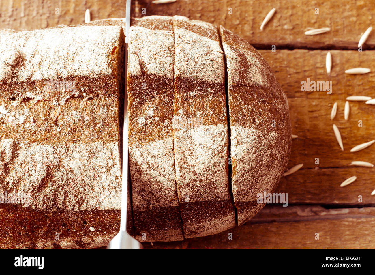 Cutting of rye bread with a knife on a wooden board Stock Photo