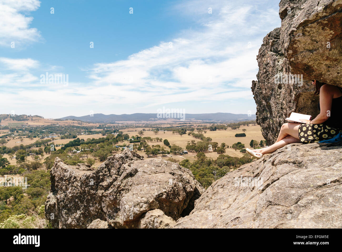 Young woman reading a book on rocky outcrop, Hanging Rock, Macedon Ranges, Victoria, Australia Stock Photo