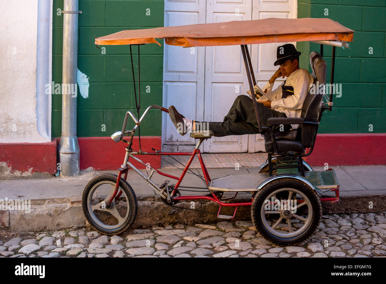 Rickshaw driver waiting for customers and reading a book, Trinidad, Sancti Spiritus Province, Cuba Stock Photo