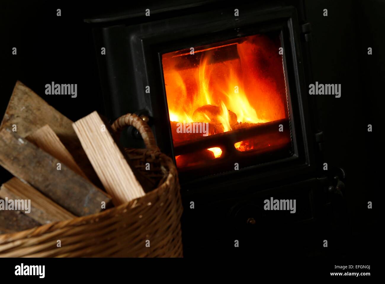 A wood burner and basket of logs. Stock Photo