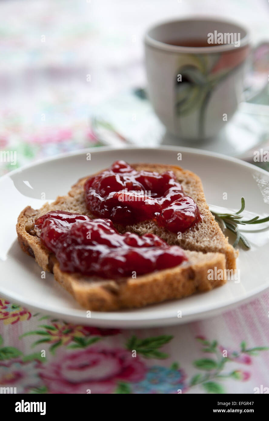 White plate with toast and jam with cup on pink tablecloth with flowers Stock Photo