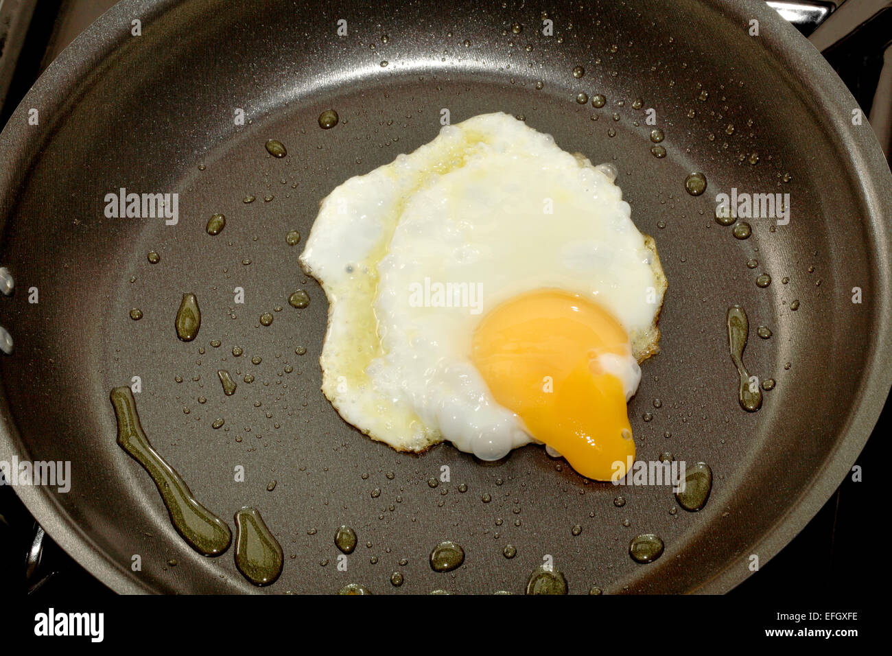 A broken fried egg in a frying pan with the yolk running out Stock Photo