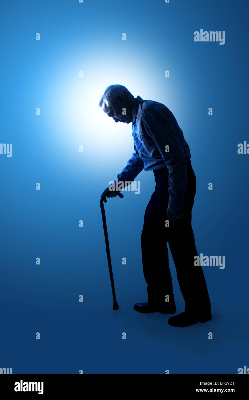 A graduated blue to white background giving a semi silhouette of a man in his sixties walking unsteadily and using a curved handled walking stick Stock Photo