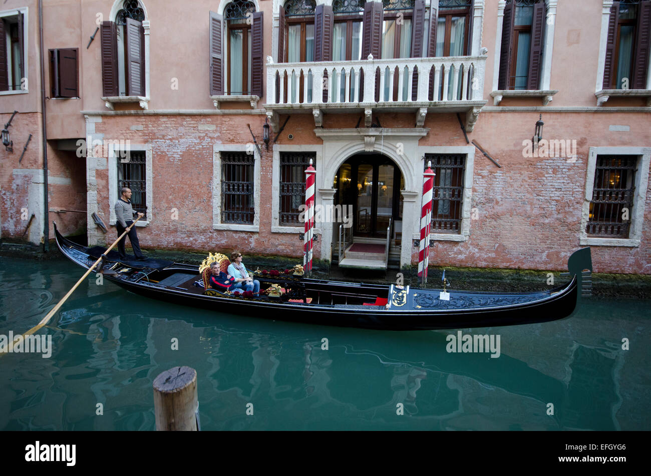 Gondolier on gondola with passengers going past an old building in Venice, Italy Stock Photo