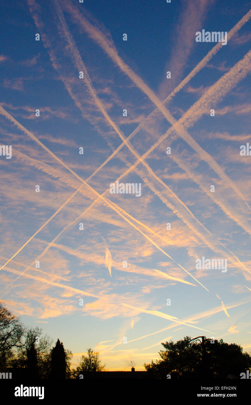 Vapour trails from planes in sky showing flight path over Midhurst Sussex UK Sunrise Stock Photo