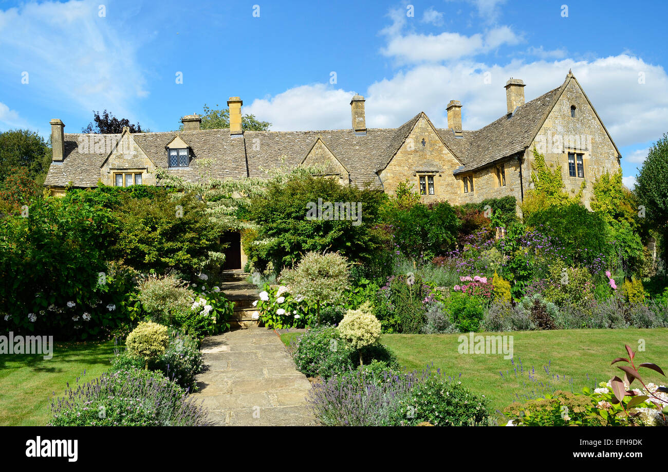 An English manor built out of Cotswold stone with stone tiles on the roof with a garden full of flowers and a grass lawn. Stock Photo