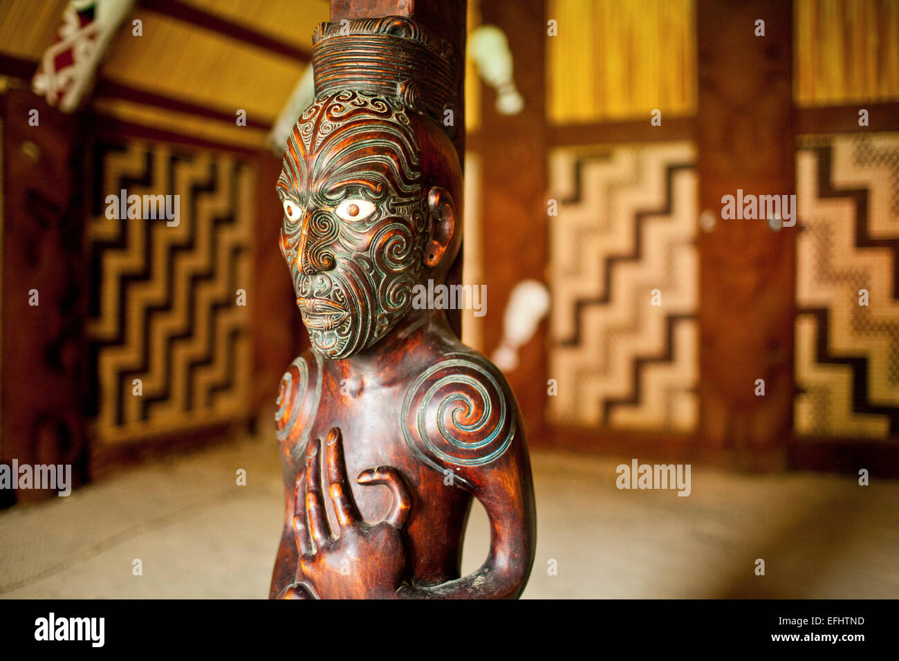 Carved wooden ancestral sculpture with spiral tatoos in the Maori traditional meeting house at Okains Bay, carved meeting house Stock Photo