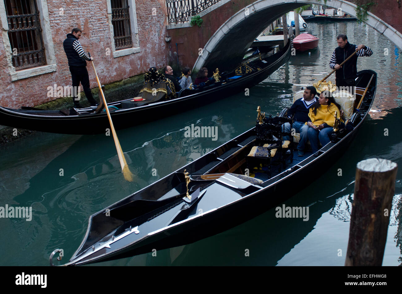 Gondoliers on two gondolas going underneath a bridge in Venice, Italy Stock Photo