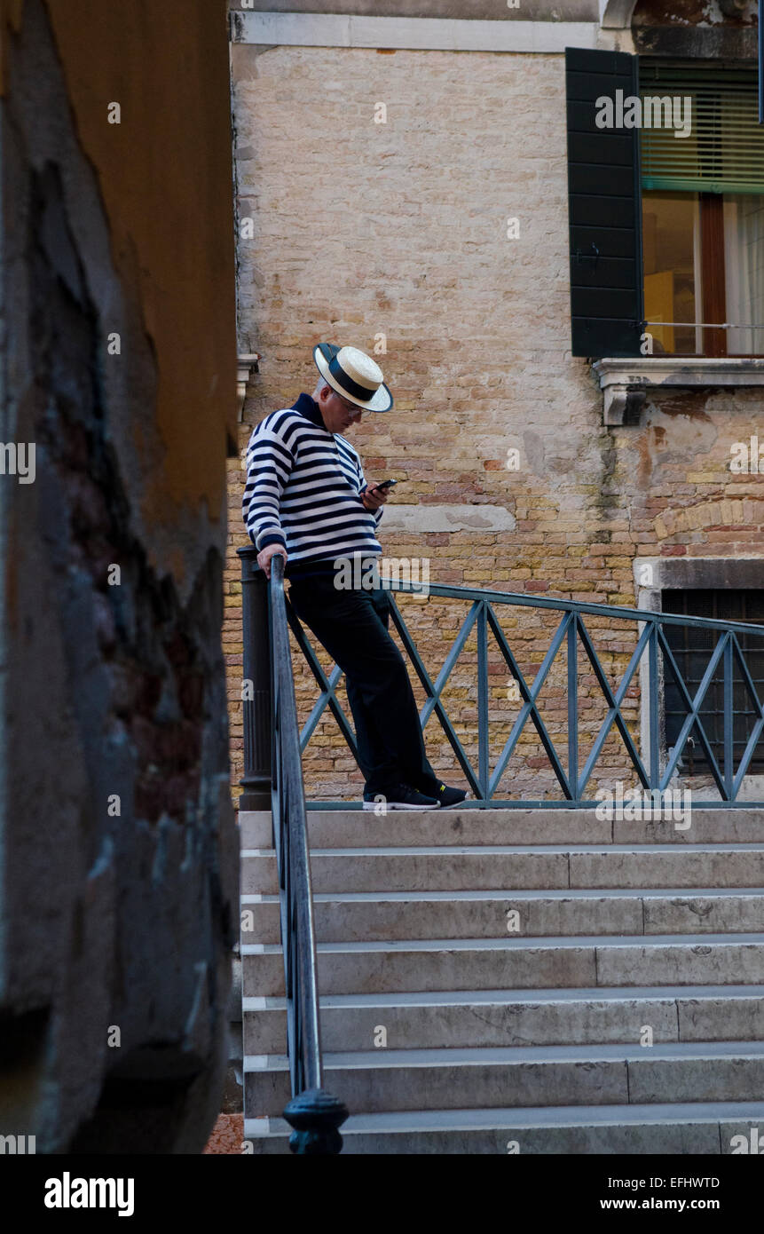 A Gondolier checking his mobile phone on a bridge in Venice, Italy Stock Photo