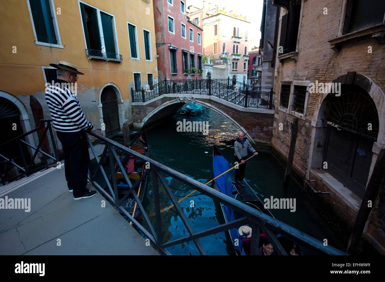Gondolier on bridge with a gondola going underneath it in Venice, Italy Stock Photo