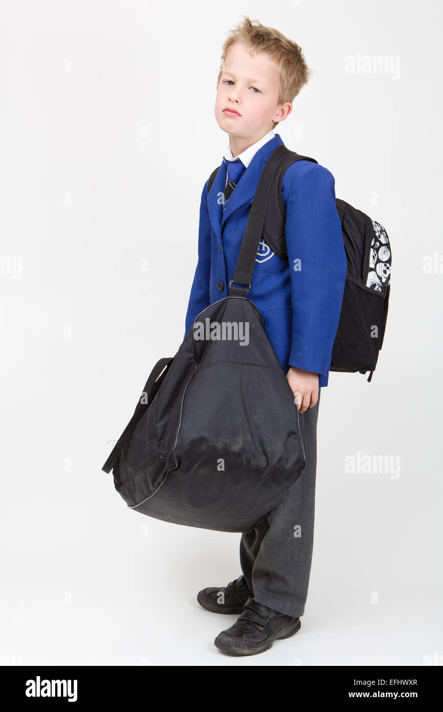 7-year-old boy in school uniform looking unhappy with heavy school bags. Photographed on a white background Stock Photo