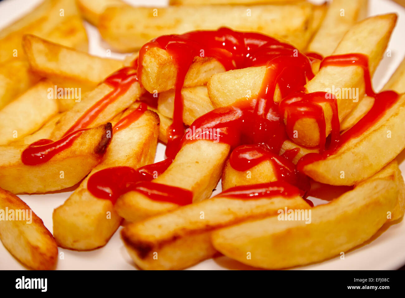 plate of cooked oven chips covered in tomato ketchup Stock Photo