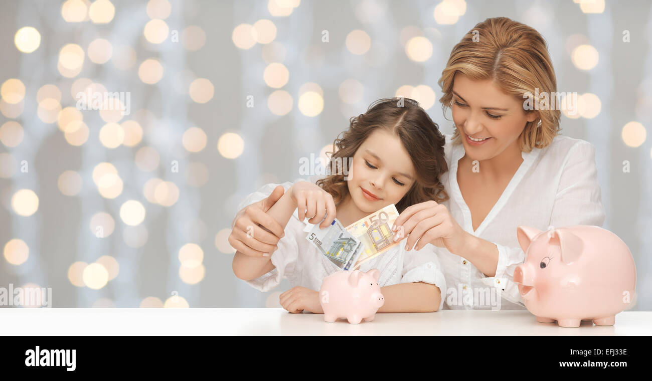 mother and daughter putting money to piggy banks Stock Photo - Alamy
