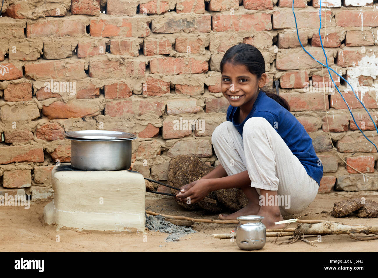 India, Uttar Pradesh, Agra, Indian girl tending to outdoor fire using buffalo dung as fuel. Stock Photo